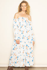 woman wearing a white off-the-shoulder floral maxi dress with blue and orange patterns and long sleeves