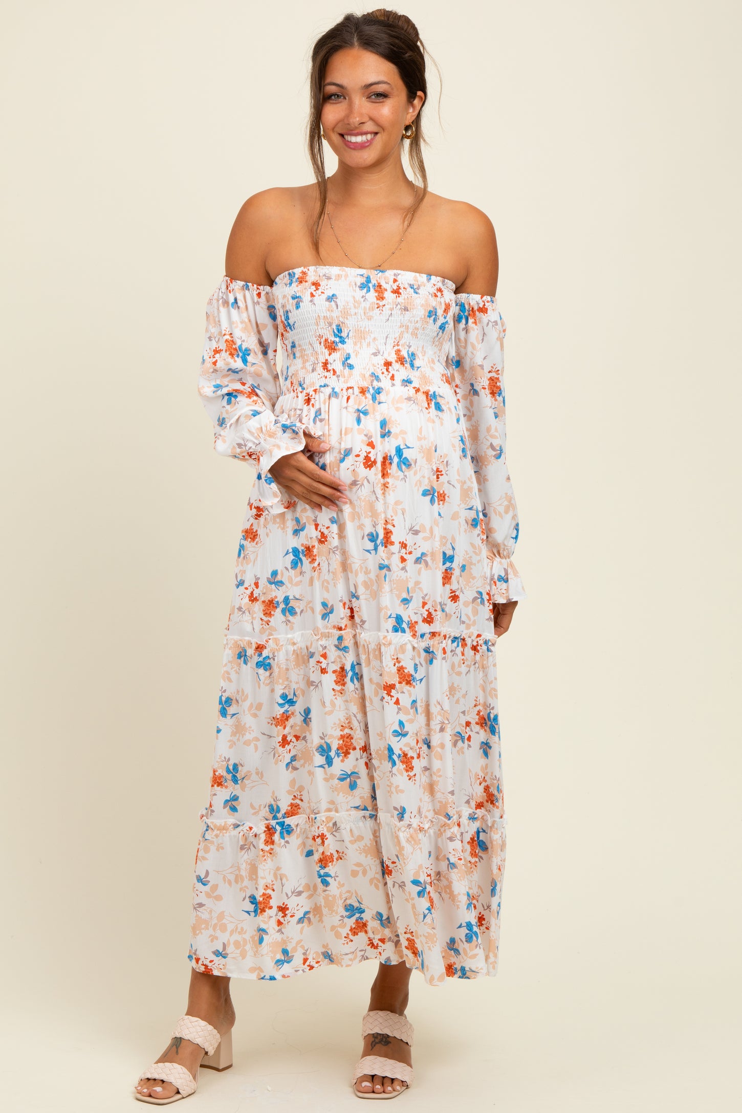 woman wearing a floral off-the-shoulder maternity dress with a flowing skirt and holding her baby bump