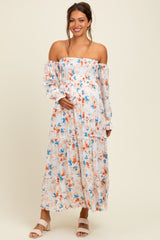 woman wearing a floral off-the-shoulder maternity dress with a flowing skirt and holding her baby bump