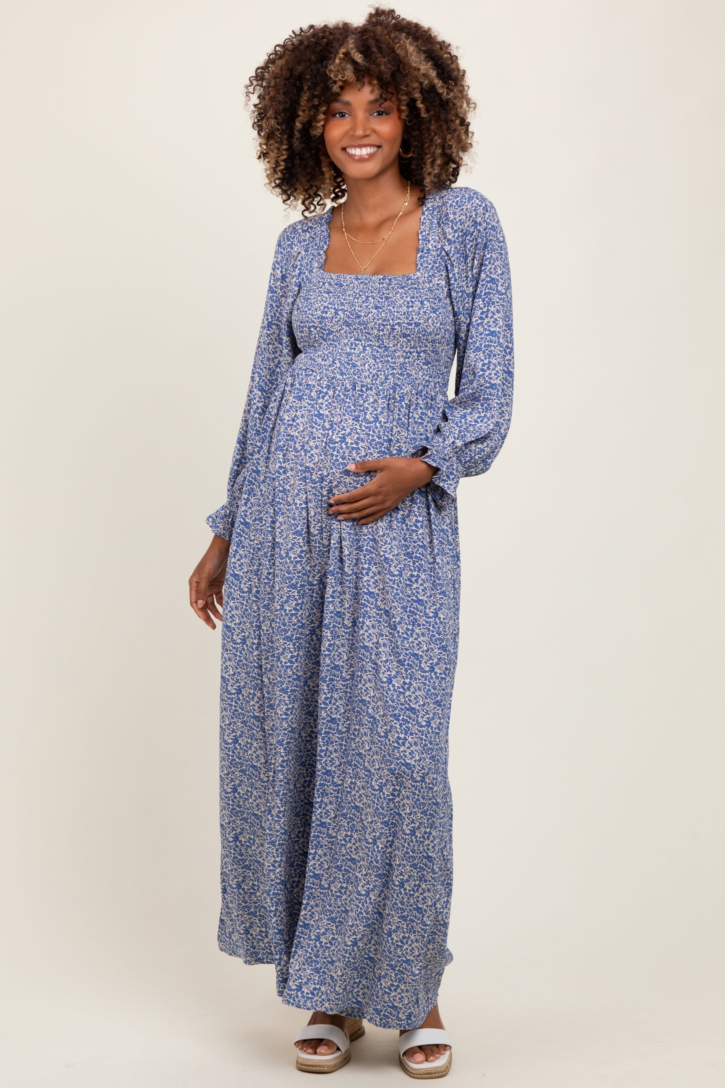 woman wearing a long blue floral maternity maxi dress and gently cradling her baby bump