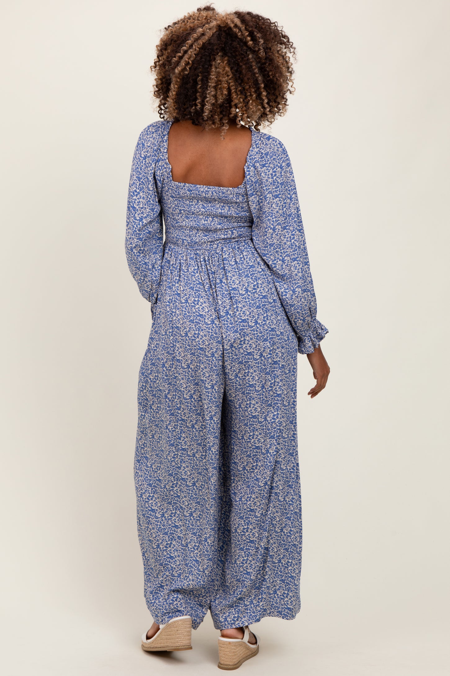 woman wearing a blue floral maternity jumpsuit with long sleeves and a square neckline, showing her baby bump