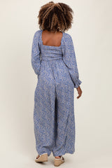 woman wearing a blue floral maternity jumpsuit with long sleeves and a square neckline, showing her baby bump