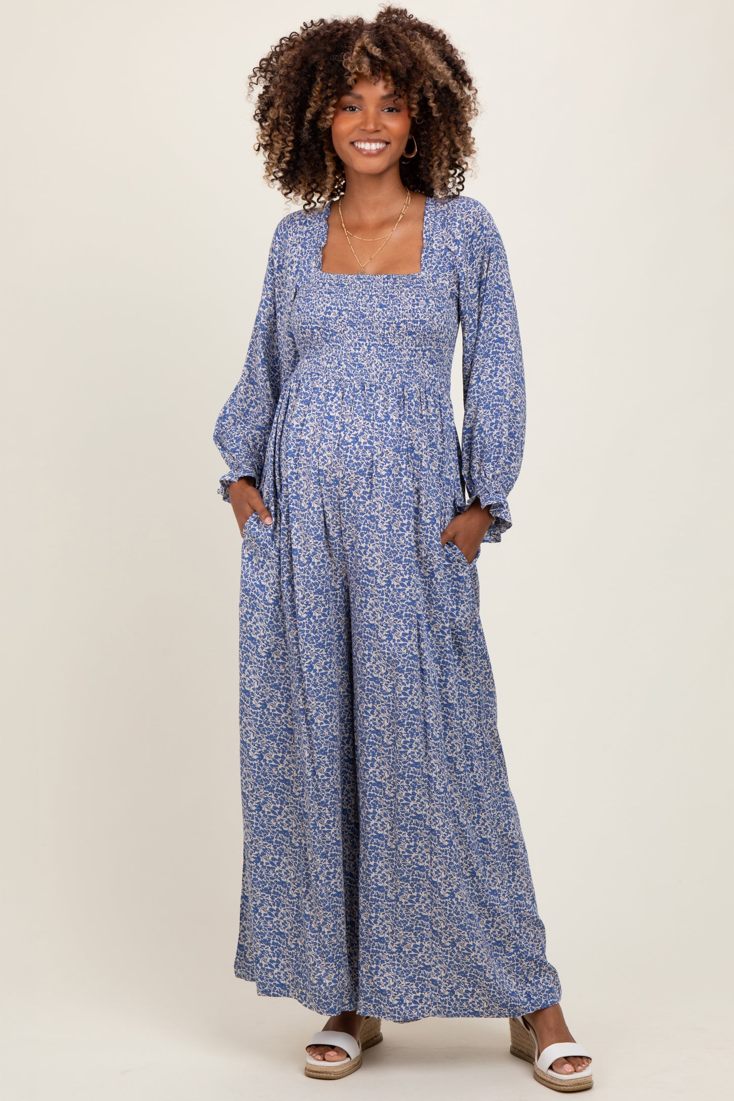woman wearing a blue floral maternity maxi dress with long sleeves and pockets, showcasing her baby bump