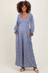 woman wearing a blue floral maternity maxi dress with long sleeves and pockets, showcasing her baby bump