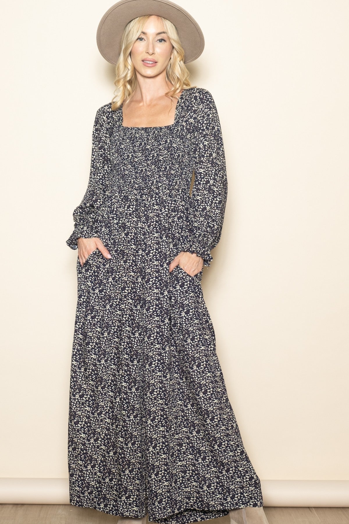 woman wearing a navy blue floral long sleeve maxi dress with a square neckline and pockets, paired with a wide-brim hat