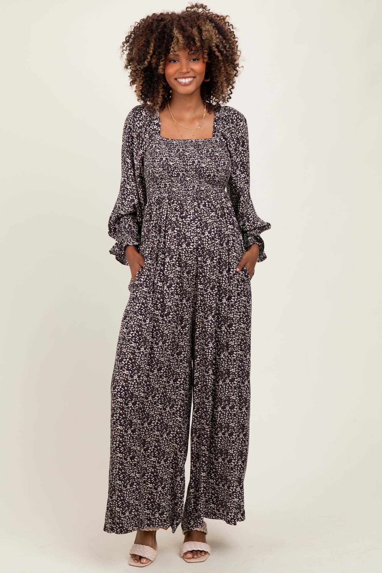 woman wearing a floral print black maternity jumpsuit with long sleeves and pockets, showing her baby bump
