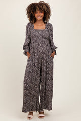 woman wearing a floral print black maternity jumpsuit with long sleeves and pockets, showing her baby bump