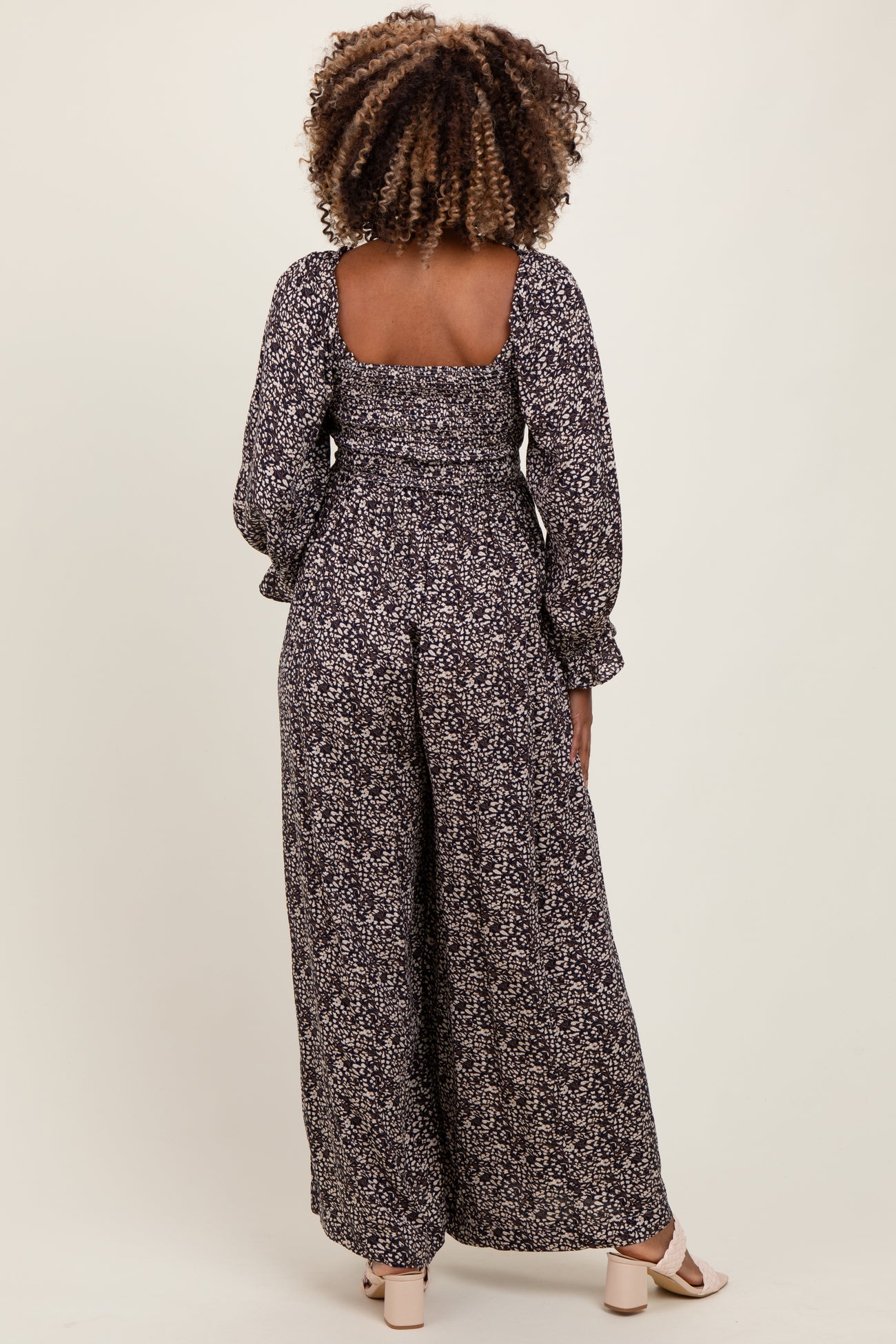 woman wearing a black and white floral print maternity jumpsuit with long sleeves and wide-leg pants, showing her baby bump
