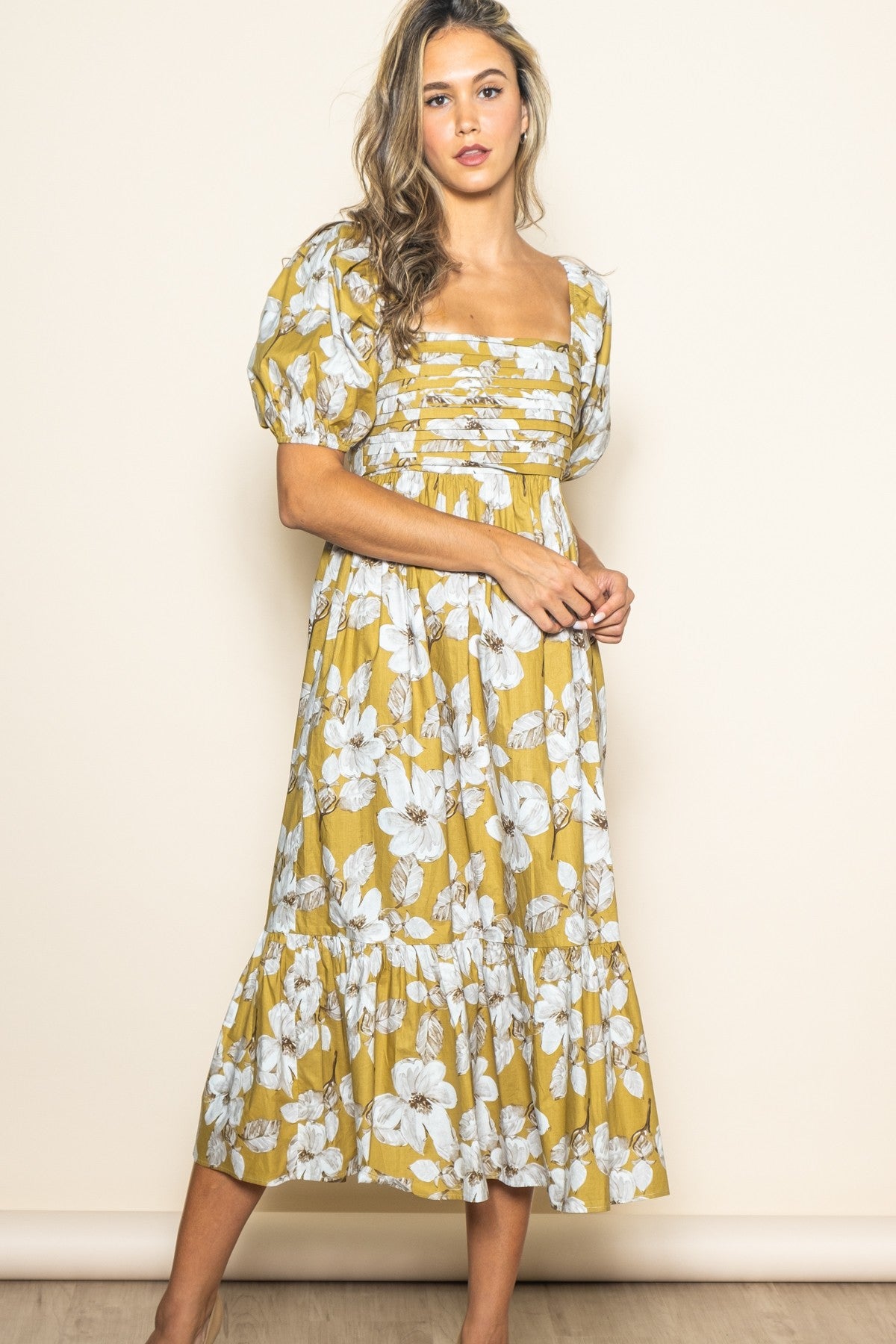 woman wearing a yellow floral midi dress with puff sleeves and a square neckline, standing against a light background
