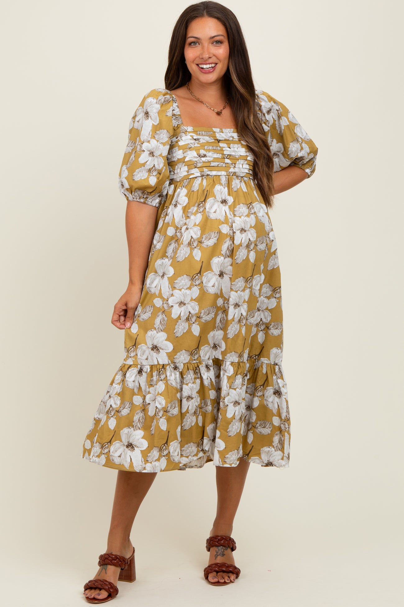 woman wearing a floral mustard maternity dress with puff sleeves and a tiered skirt, showcasing her baby bump