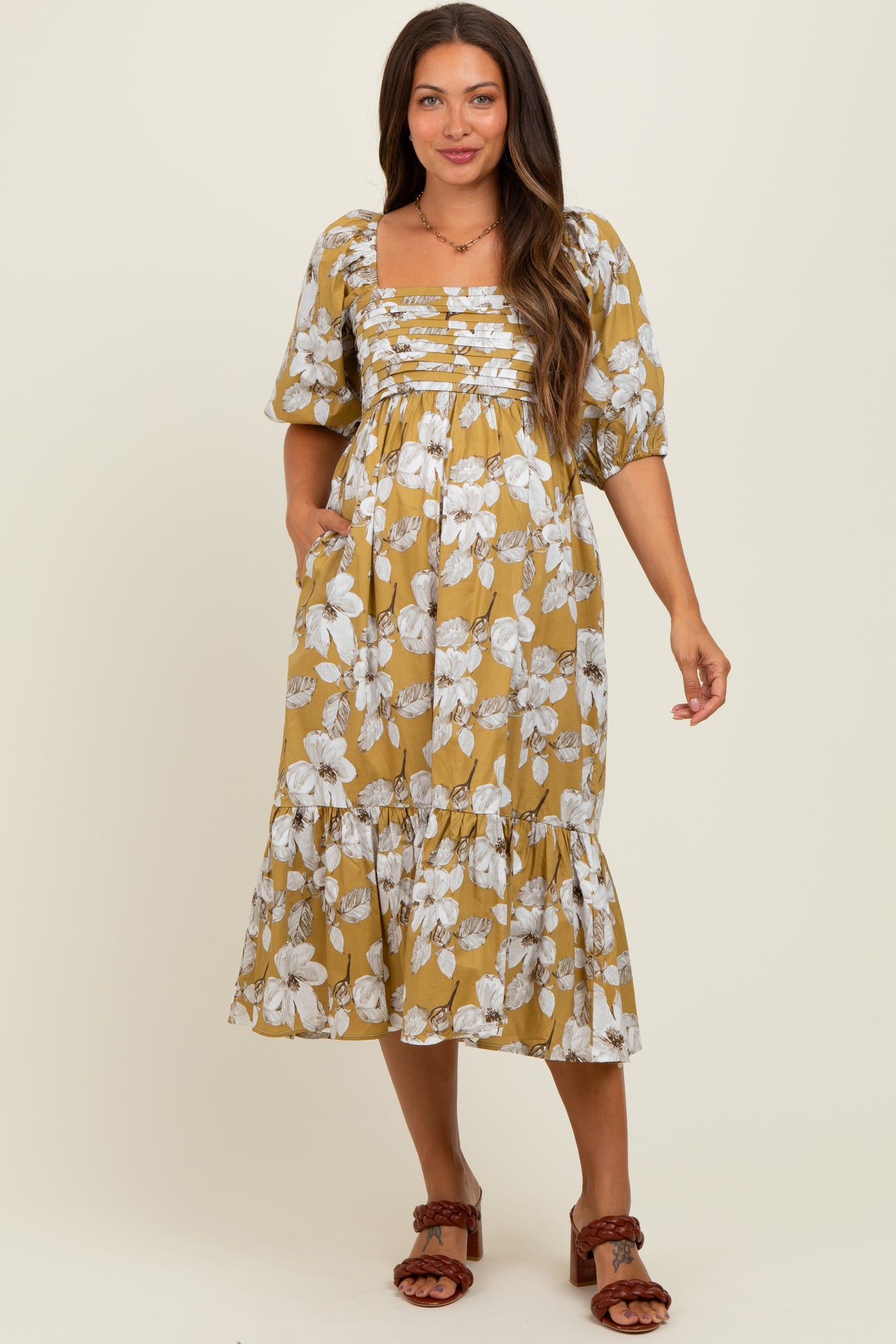 woman wearing a mustard floral print maternity dress with puff sleeves and a tiered hemline