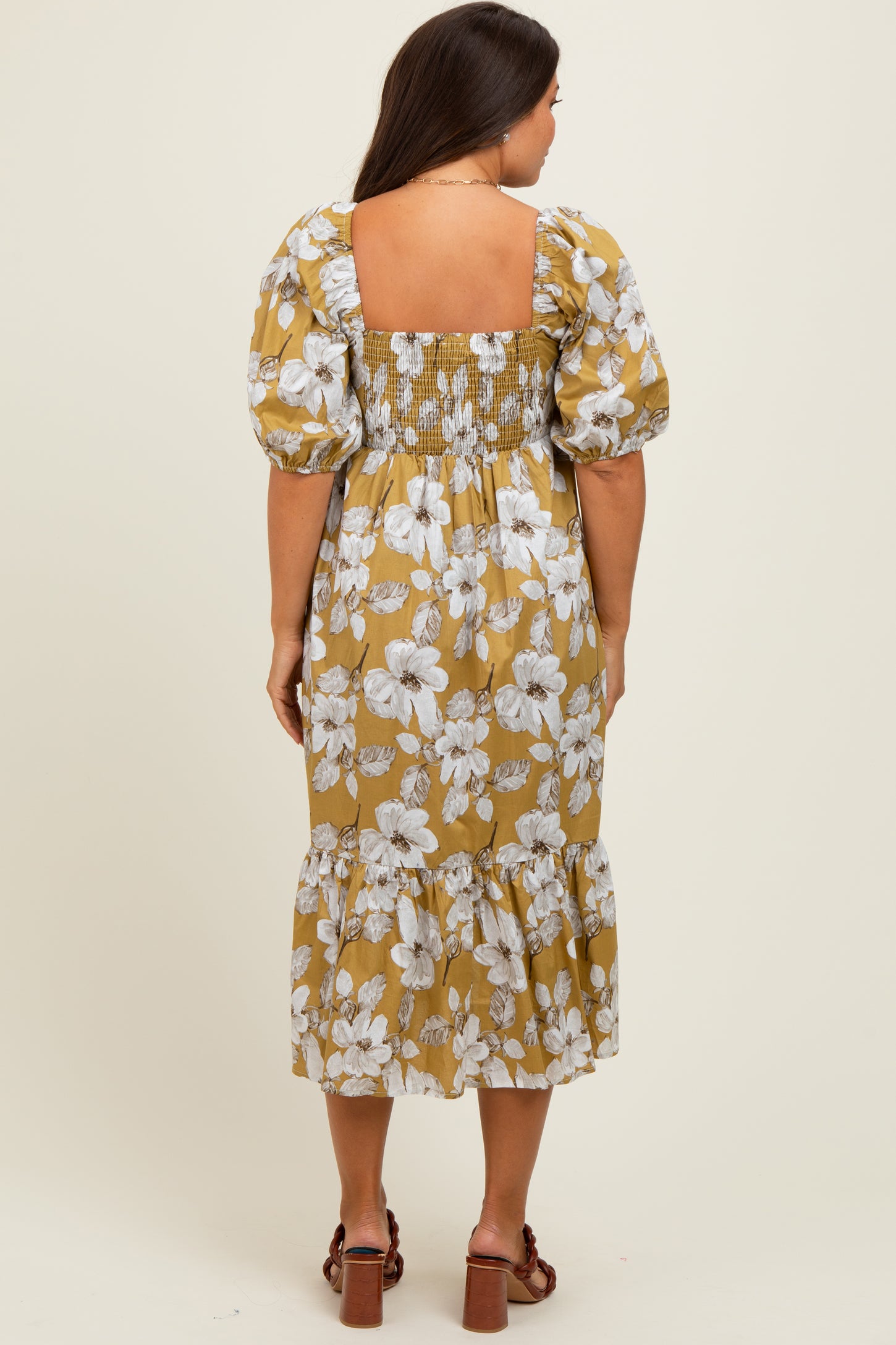 woman wearing a mustard floral maternity dress with puff sleeves and a tiered hem, showing a visible baby bump from the back