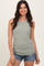 woman wearing a light green ribbed sleeveless top and denim shorts, smiling against a neutral background