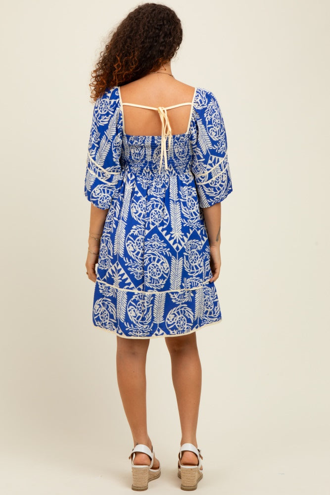 woman wearing a blue and white patterned maternity dress with puff sleeves and an open back design
