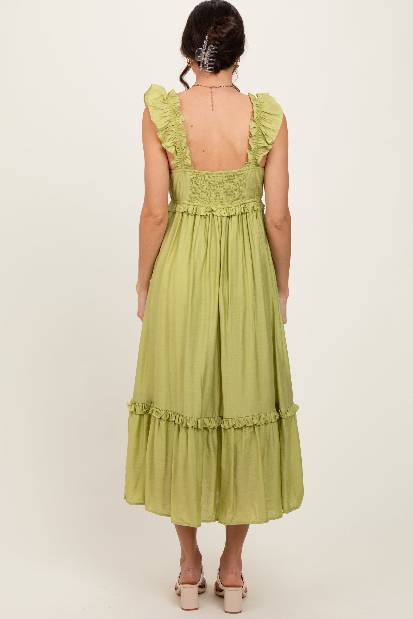woman wearing a pale green sleeveless dress with ruffled straps and a tiered skirt, seen from the back