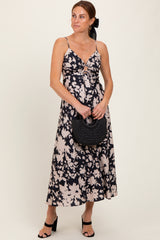 woman wearing a sleeveless navy floral midi dress with a front knot detail, holding a black woven handbag