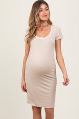 woman wearing a beige maternity dress with short sleeves and a bow detail at the neckline, showing her baby bump