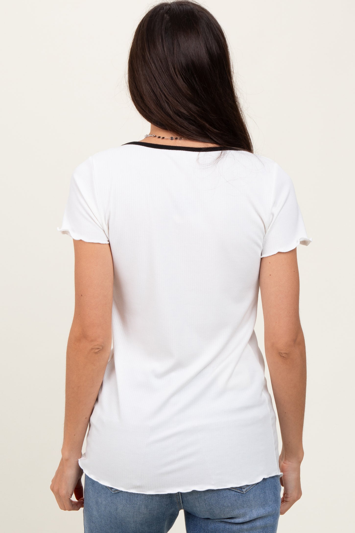 woman wearing a white short sleeve top with a black neckline and a relaxed fit, viewed from the back