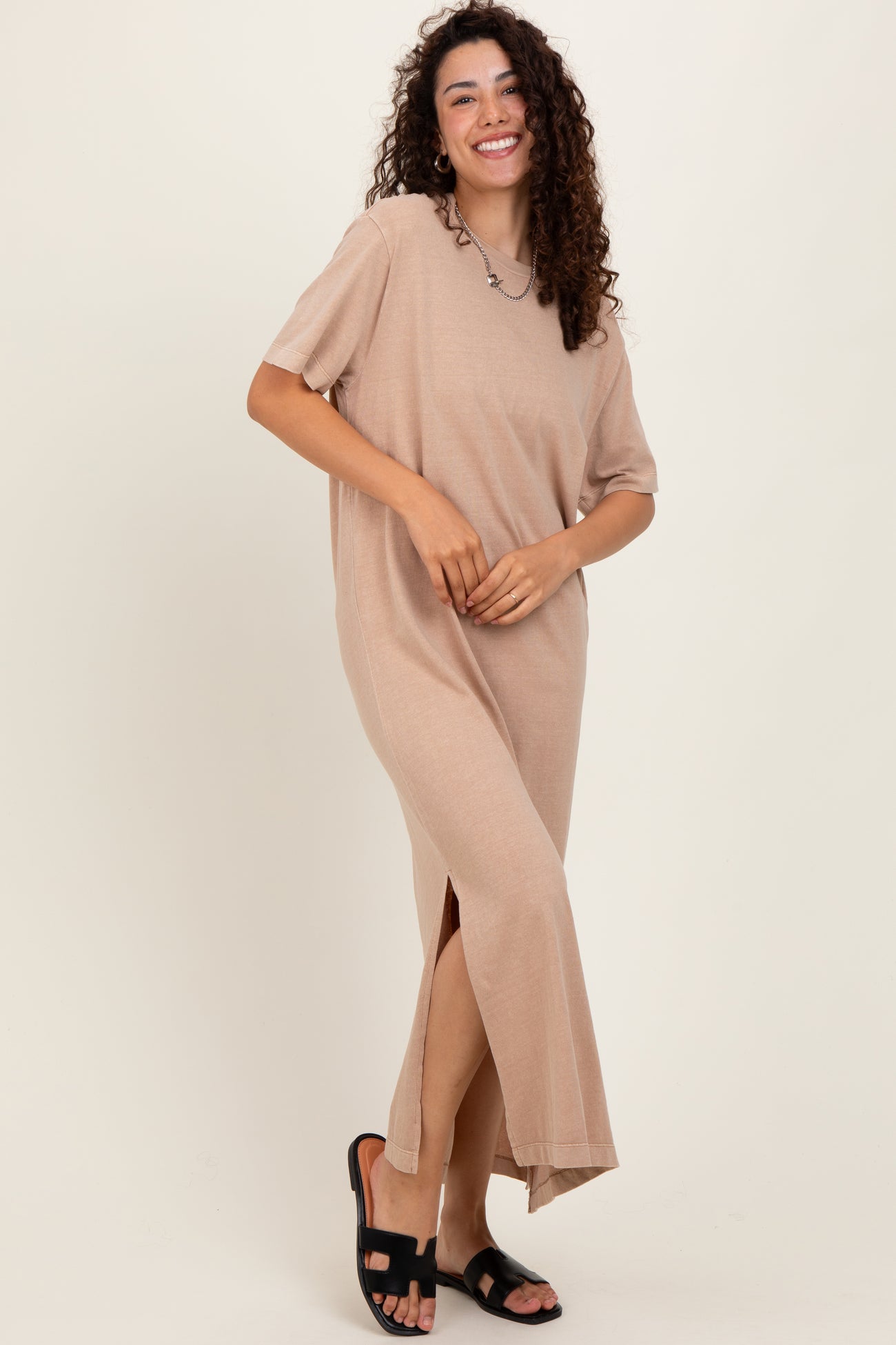 woman wearing a beige short sleeve maxi dress with side slits and standing in black sandals