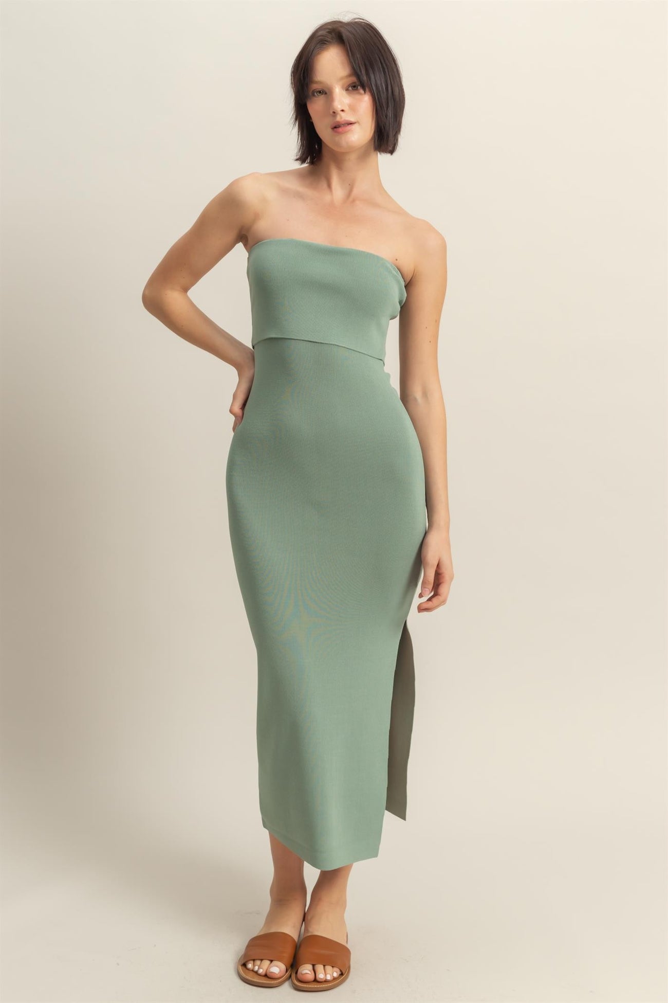 woman wearing a sage green strapless midi dress with a side slit and a fitted silhouette