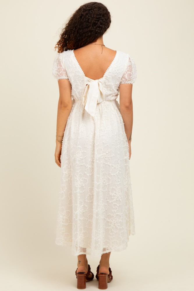 woman wearing a white lace maternity dress with a tied back detail and short puff sleeves