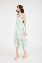 woman wearing a floral green and white midi dress with adjustable straps and a tiered skirt