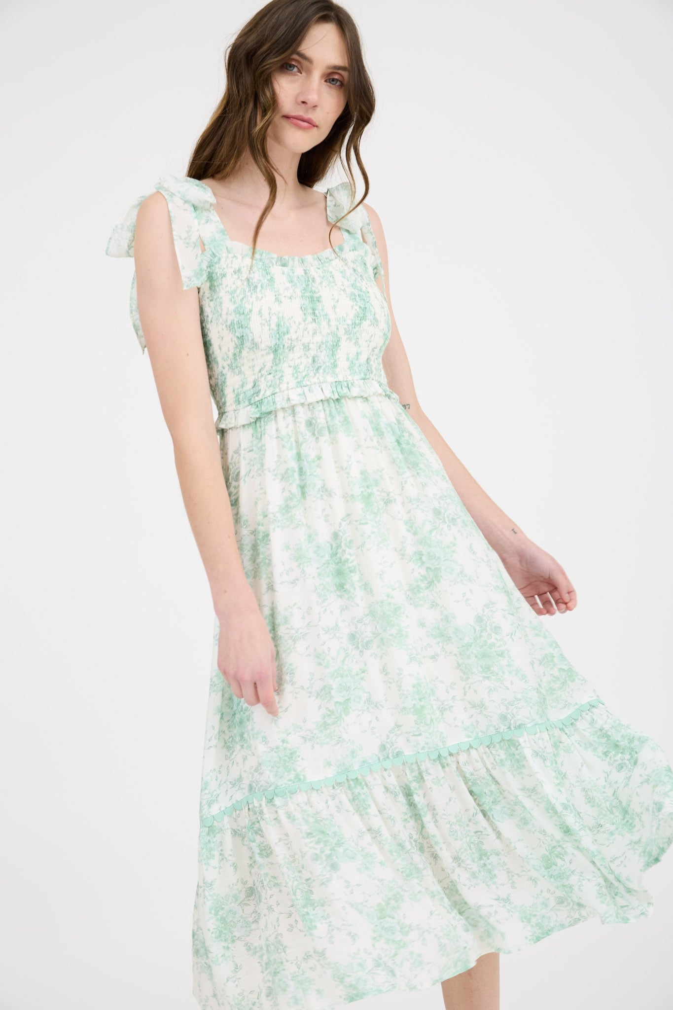 woman wearing a floral print midi dress in green and white with ruffled straps and a tiered skirt