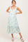 woman wearing a green floral print maternity dress with ruffled straps and a tiered skirt, smiling against a neutral background
