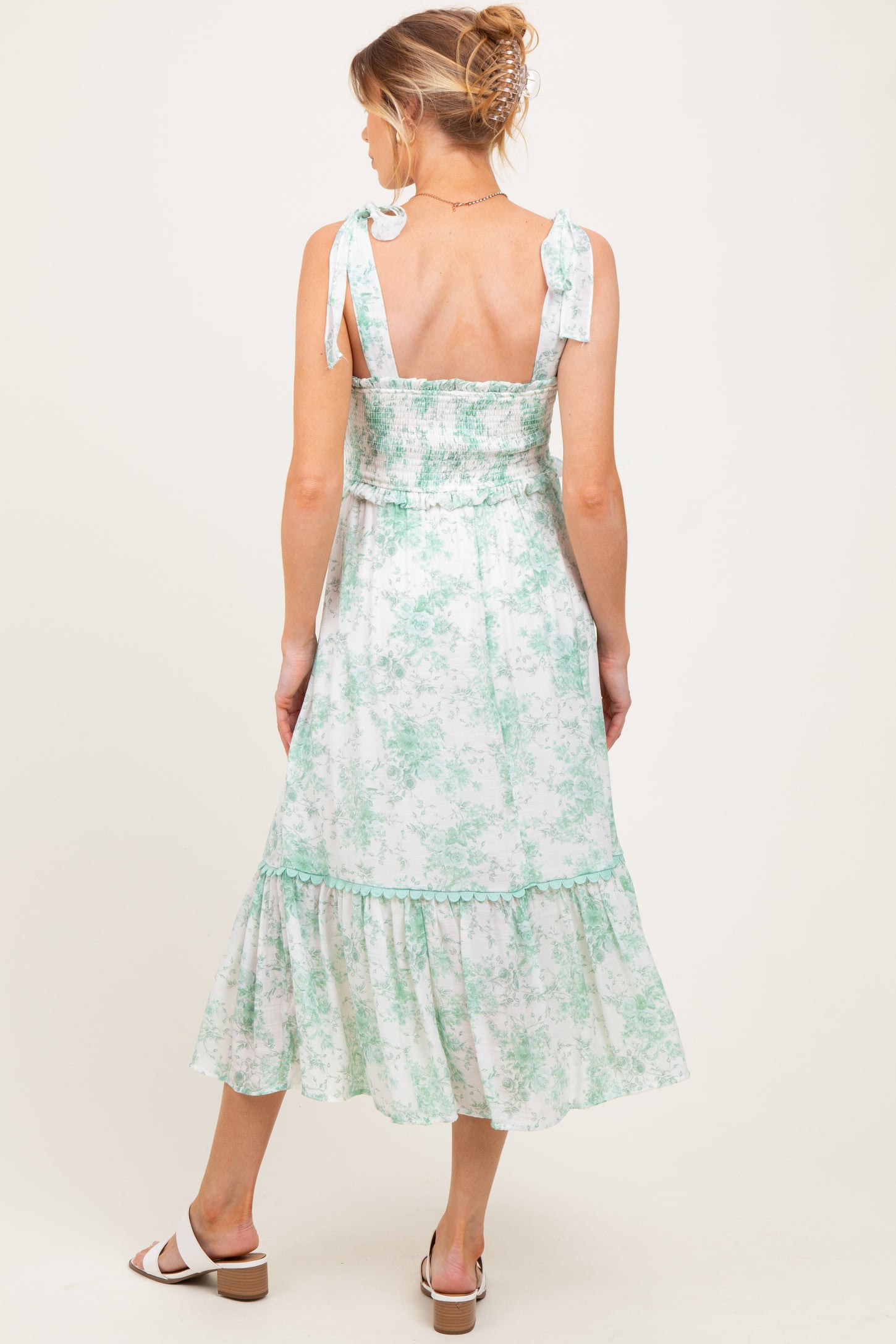 woman wearing a green and white floral print maternity dress with tie straps and a tiered hem, showing her baby bump