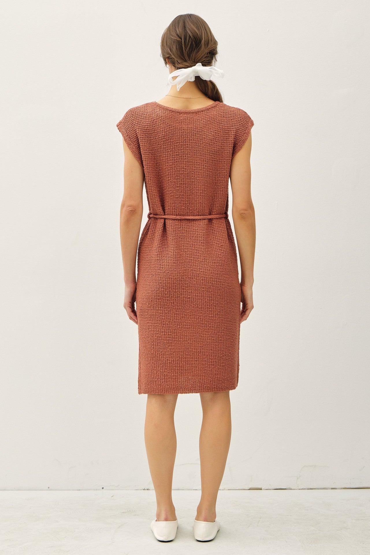 woman wearing a rust-colored knitted dress with a belted waist and short sleeves, viewed from the back