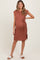 woman wearing a rust-colored knitted maternity dress with a tie belt and side slits, showcasing her baby bump