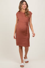 woman wearing a rust-colored knitted maternity dress with a tie waist and short sleeves, showcasing her baby bump