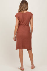 woman wearing a rust-colored short sleeve maternity dress with a belted waist and a knee-length hemline