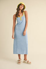 woman wearing a light blue sleeveless maxi dress with yellow straps and buttons, paired with a matching yellow bucket hat
