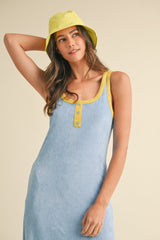 woman wearing a light blue tank dress with yellow trim and buttons, paired with a yellow bucket hat