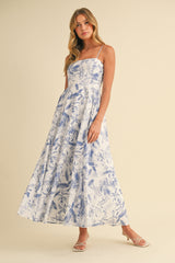 woman wearing a white floral maxi dress with blue patterns and thin straps, standing against a light background