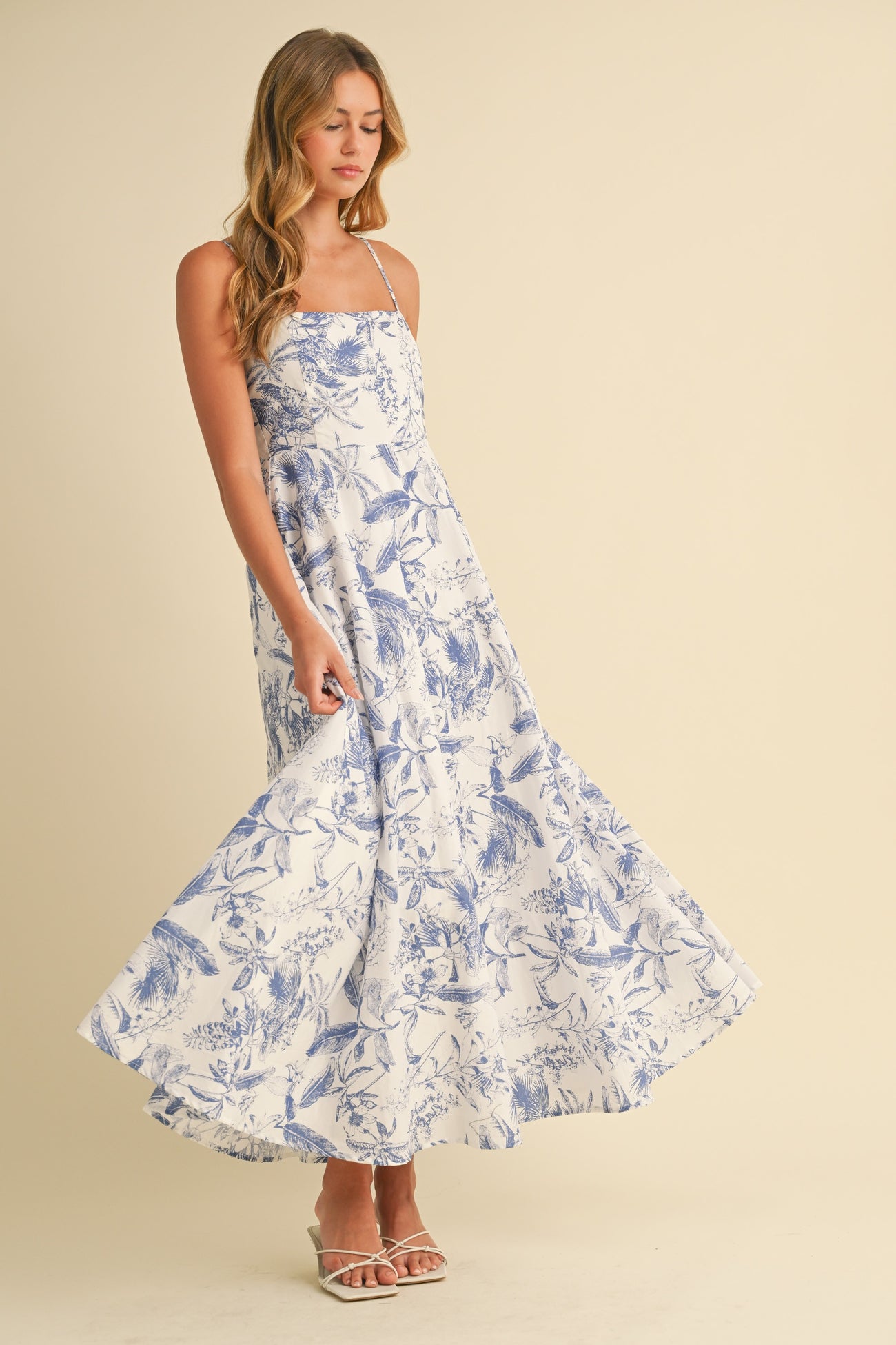 woman wearing a white floral maxi dress with blue print and spaghetti straps, twirling in the dress