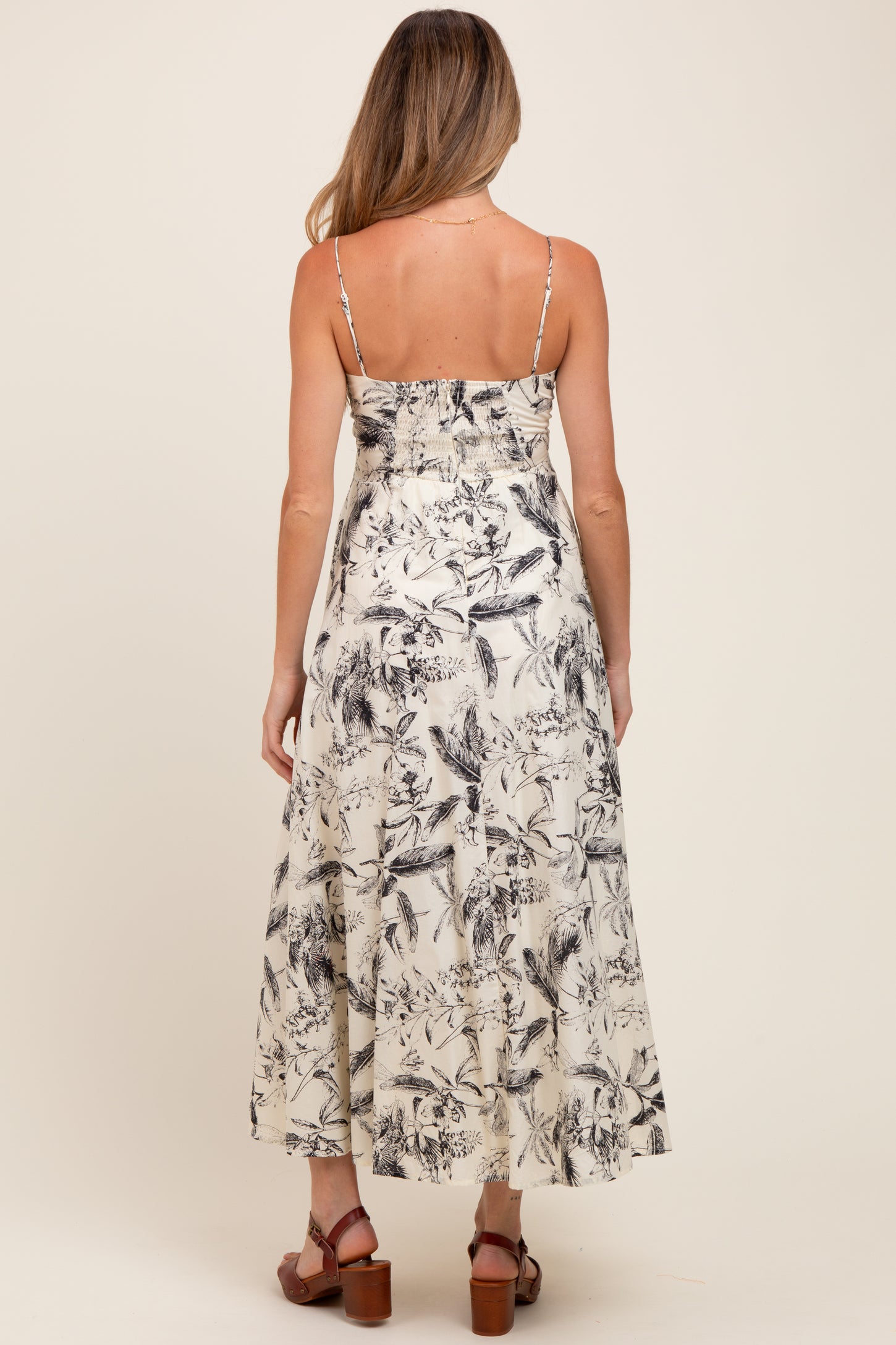 woman wearing a floral print maternity maxi dress with adjustable straps and a flowing skirt, showing her baby bump
