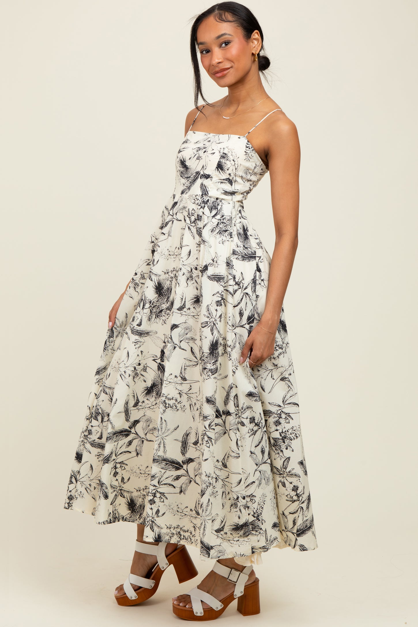 woman wearing a flowy white maxi dress with black floral print and strappy sandals