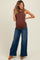 woman wearing a brown ribbed maternity tank top and blue wide-leg jeans, showing her baby bump
