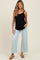 woman wearing a black maternity tank top and light blue wide-leg jeans, showing her baby bump