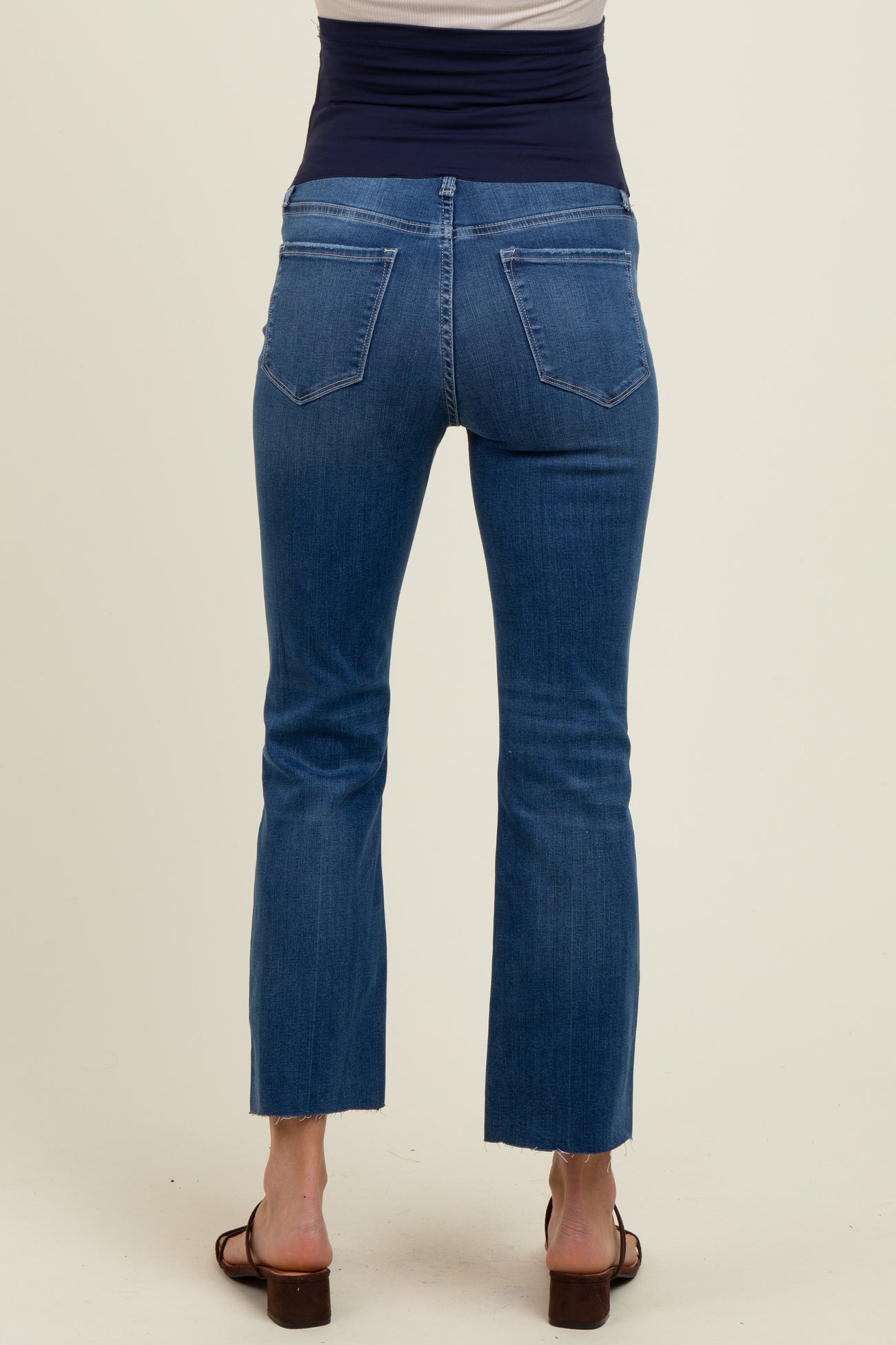 woman wearing a back view of dark wash maternity jeans with a cropped flare leg design