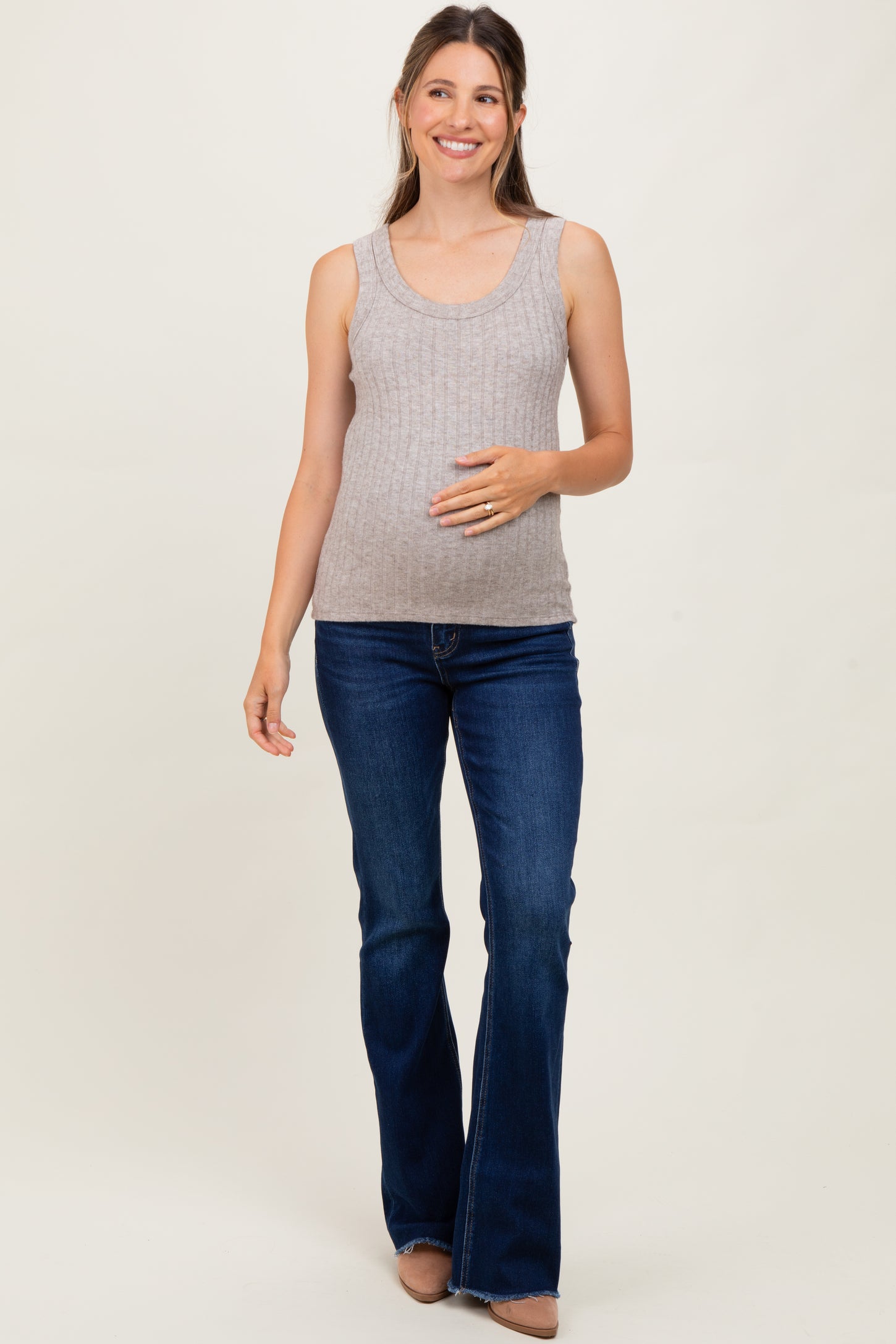 woman wearing a light gray ribbed maternity tank top and blue flared jeans, holding her baby bump