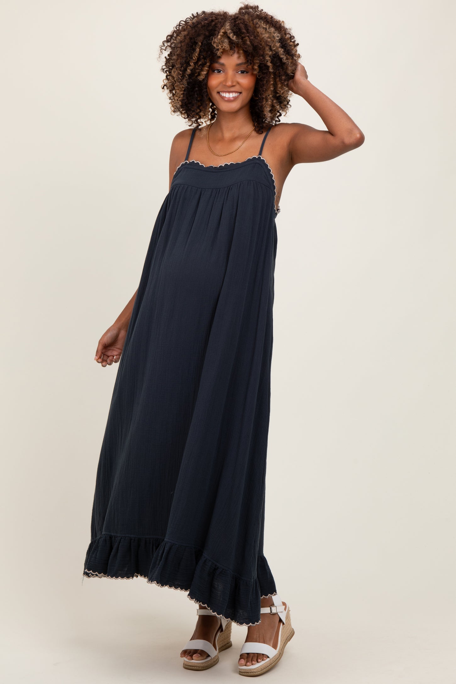 woman wearing a navy blue maternity maxi dress with adjustable straps and ruffle hem, highlighting her baby bump
