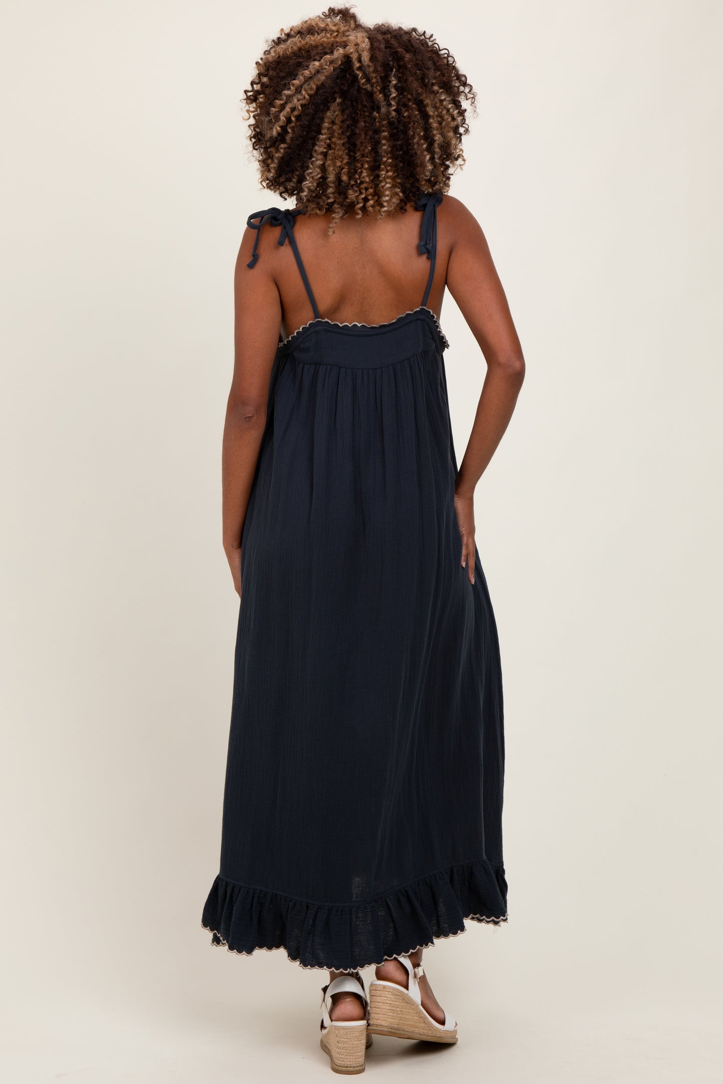 woman wearing a navy blue maternity maxi dress with adjustable straps and ruffled hem, showing off her baby bump