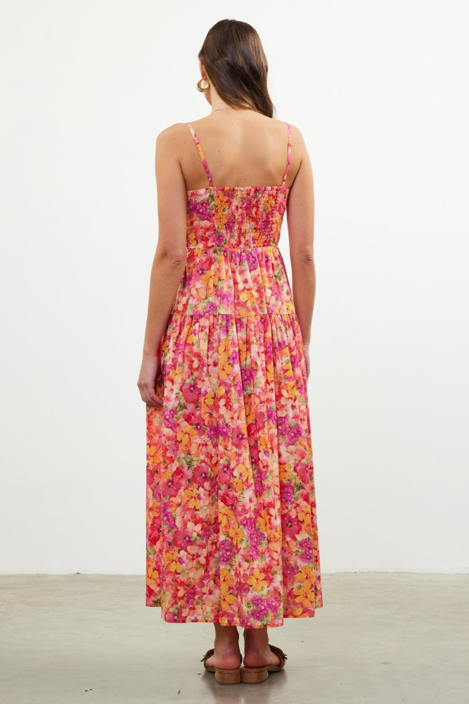 woman wearing a pink floral maxi dress with a smocked back and adjustable straps, showing a vibrant multicolor pattern