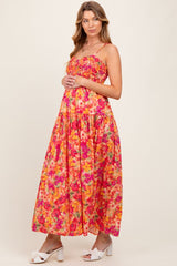 woman wearing a pink floral maternity maxi dress with a fitted bodice and flowing skirt, holding her baby bump