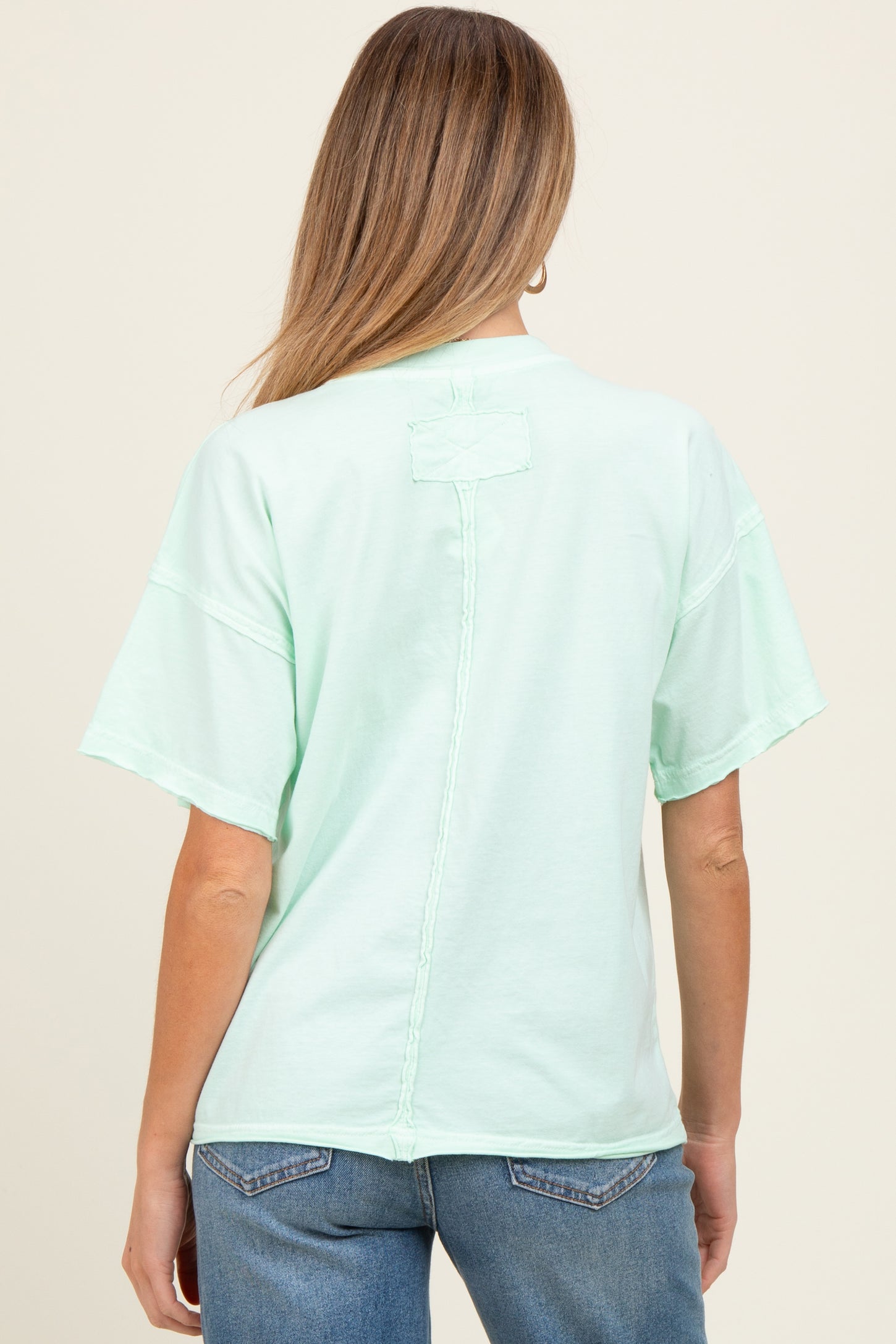 woman wearing a mint green short sleeve maternity top with a relaxed fit and a seam detail on the back