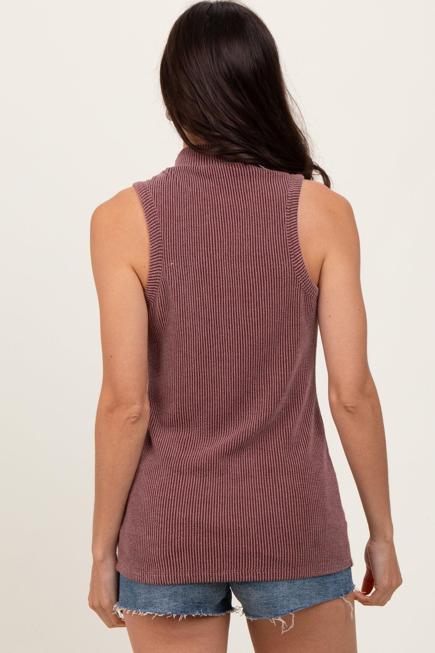 woman wearing a sleeveless ribbed maroon top and denim shorts, viewed from the back