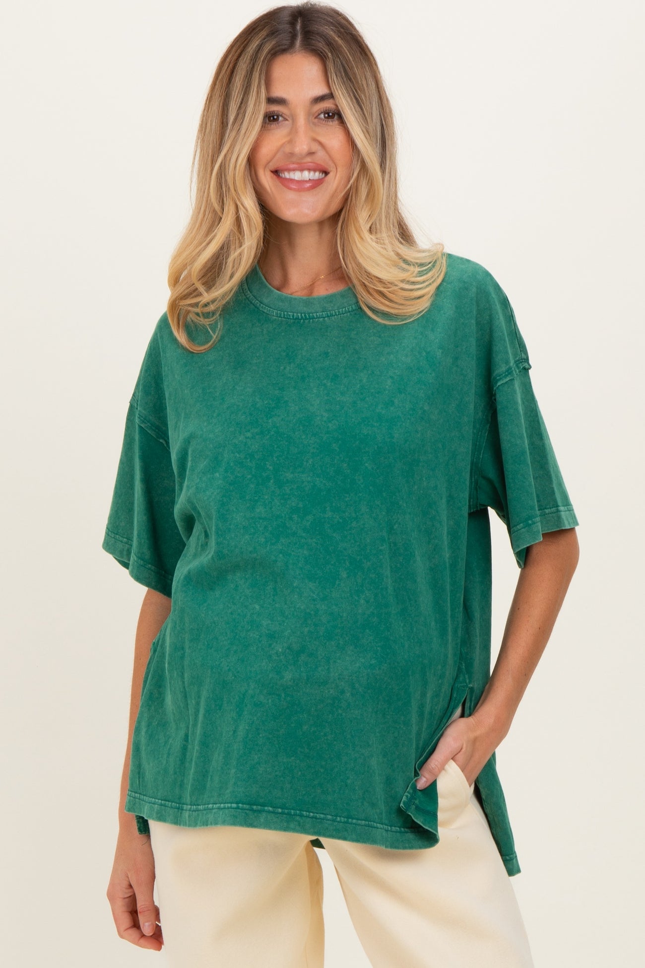 woman wearing a green oversized maternity t-shirt with short sleeves and a relaxed fit, posing with one hand in pocket